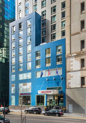 Un hotel moderno con fachada azul, múltiples ventanas y banderas.