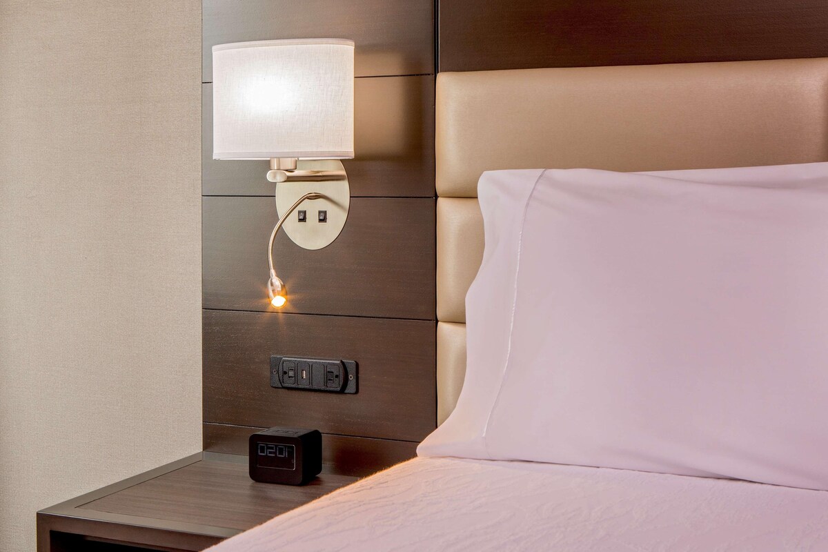 Un lit bien fait, avec un oreiller blanc et une tête de lit agrémentée d’une lampe.