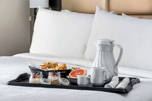 Ein ordentlich angerichtetes Frühstücksbrettchen auf einem Bett mit Gebäck, einer Grapefruit und einer Karaffe.