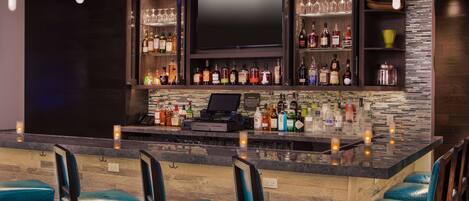 A bar area with a counter, bar stools, a television, and shelves with bottles.