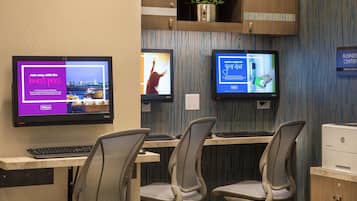 Un espacio de trabajo en un hotel con dos monitores, un teclado y sillas de oficina.