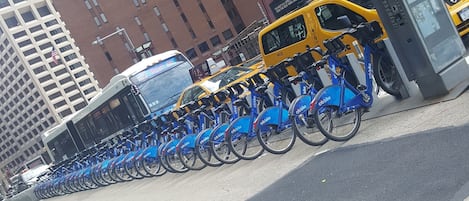 Una fila de estaciones de alquiler de Citi Bike en un entorno urbano, con edificios altos al fondo.