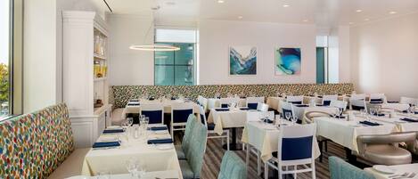 A restaurant with multiple dining tables, chairs, and a colorful patterned bench.