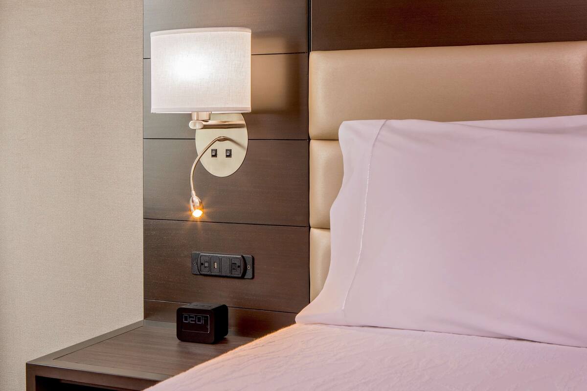 Una cama bien hecha con una almohada blanca y un cabecero con una lámpara.