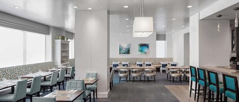A modern dining area with multiple tables and chairs, a bar area, and a patterned wall backsplash.