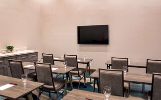 Uma sala de conferências com várias mesas e cadeiras, uma TV de tela plana na parede e uma pequena planta no balcão.