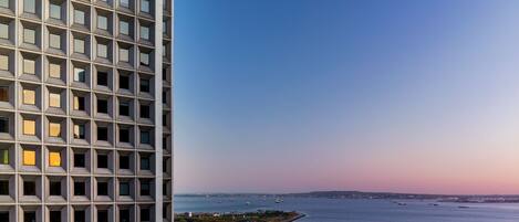 A high-rise building with a grid-like facade and a view of a calm body of water with boats.