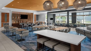 Un hall d’hôtel moderne doté d’un bar central, de plusieurs espaces aménagés pour s’asseoir et de grandes fenêtres offrant une vue sur l’extérieur.