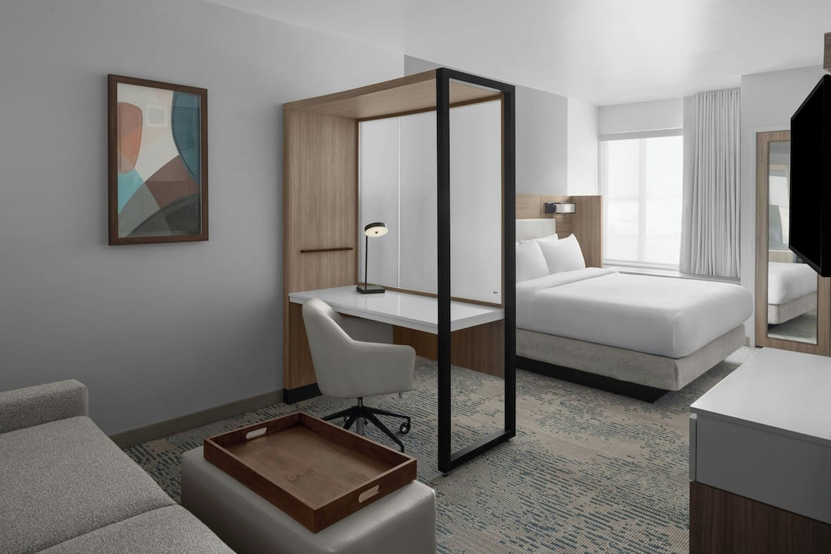 Ein modernes Hotelzimmer mit Schreibtisch, Bett, Stuhl und einem großen Spiegel.