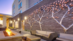 Un espace extérieur aménagé avec des sièges, un foyer et une fresque murale représentant un arbre.