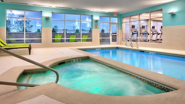 Une piscine intérieure à l’eau d’un bleu limpide, avec des chaises vertes et du matériel d’exercice.
