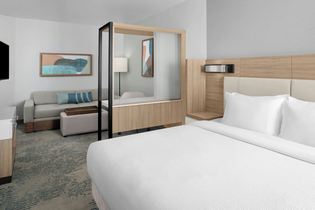 Ein modernes Hotelzimmer mit einem großen Bett, einer Couch, einem Schreibtisch und einem Spiegel.