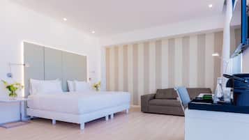 A modern hotel room with a large bed, a sofa, a desk with a laptop, and a TV.
