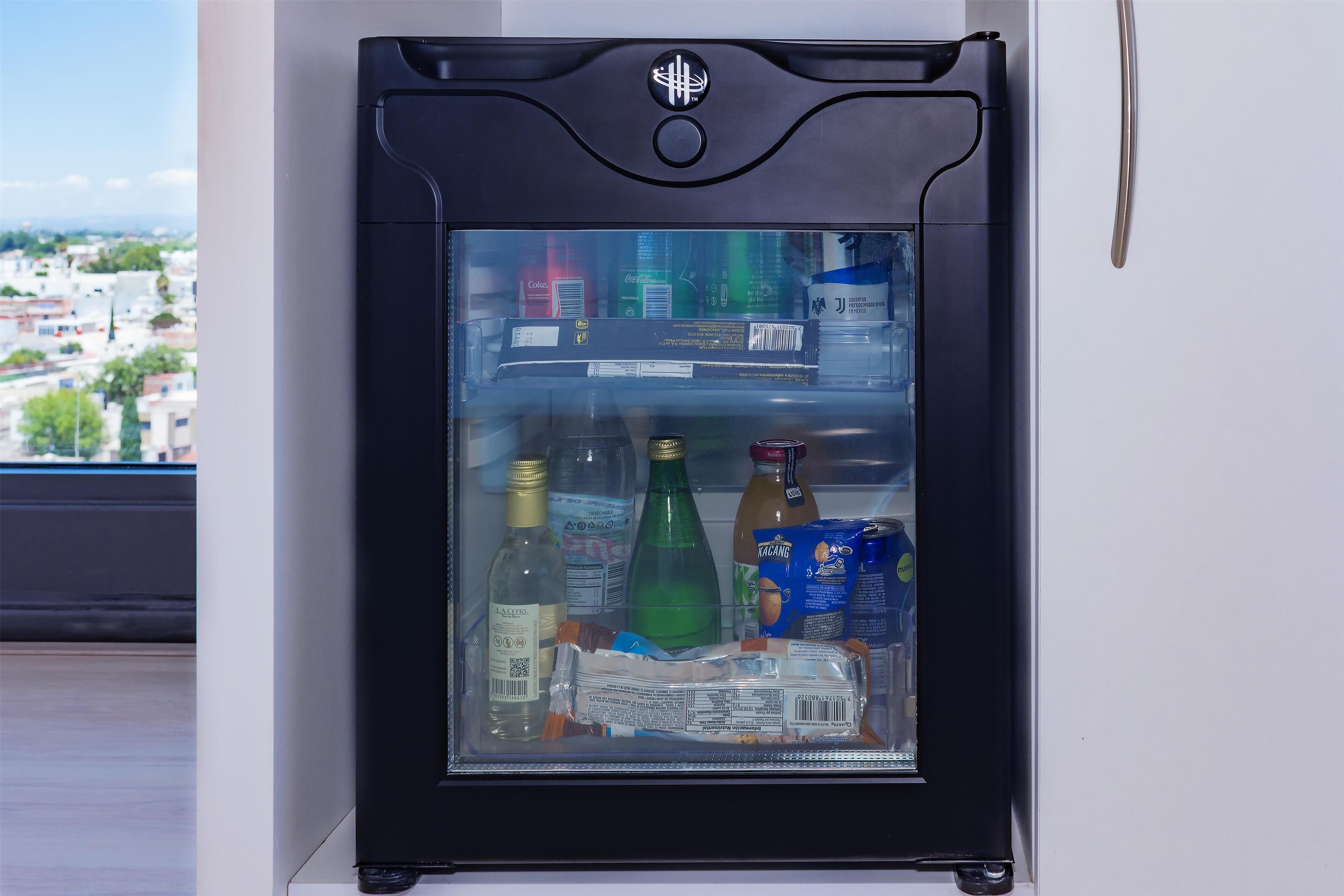 Un mini refrigerador con puerta transparente, que contiene diversas bebidas y aperitivos.