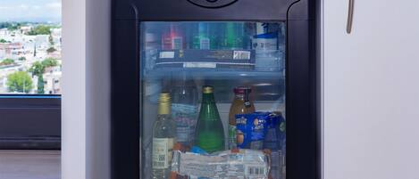 Un mini refrigerador con puerta transparente, que contiene diversas bebidas y aperitivos.
