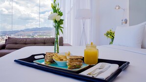 A neatly arranged breakfast tray on a bed with a city view, a vase of flowers, and a lamp. - NH San Luis Potosi (San Luis Potosi)