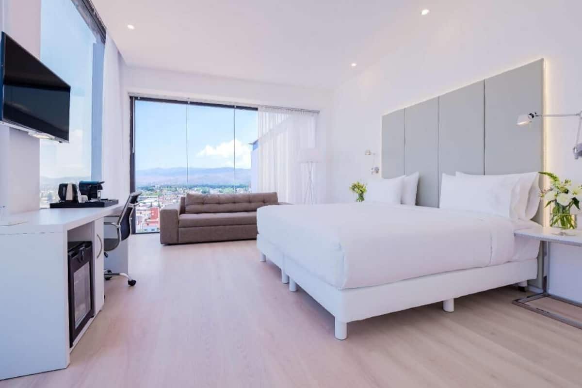 A modern hotel room with a large bed, a sofa, a desk with a computer, and a TV.