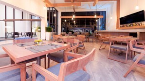 A modern dining area with wooden tables and chairs, large windows, and a flat-screen TV mounted on the wall. - NH San Luis Potosi (San Luis Potosi)