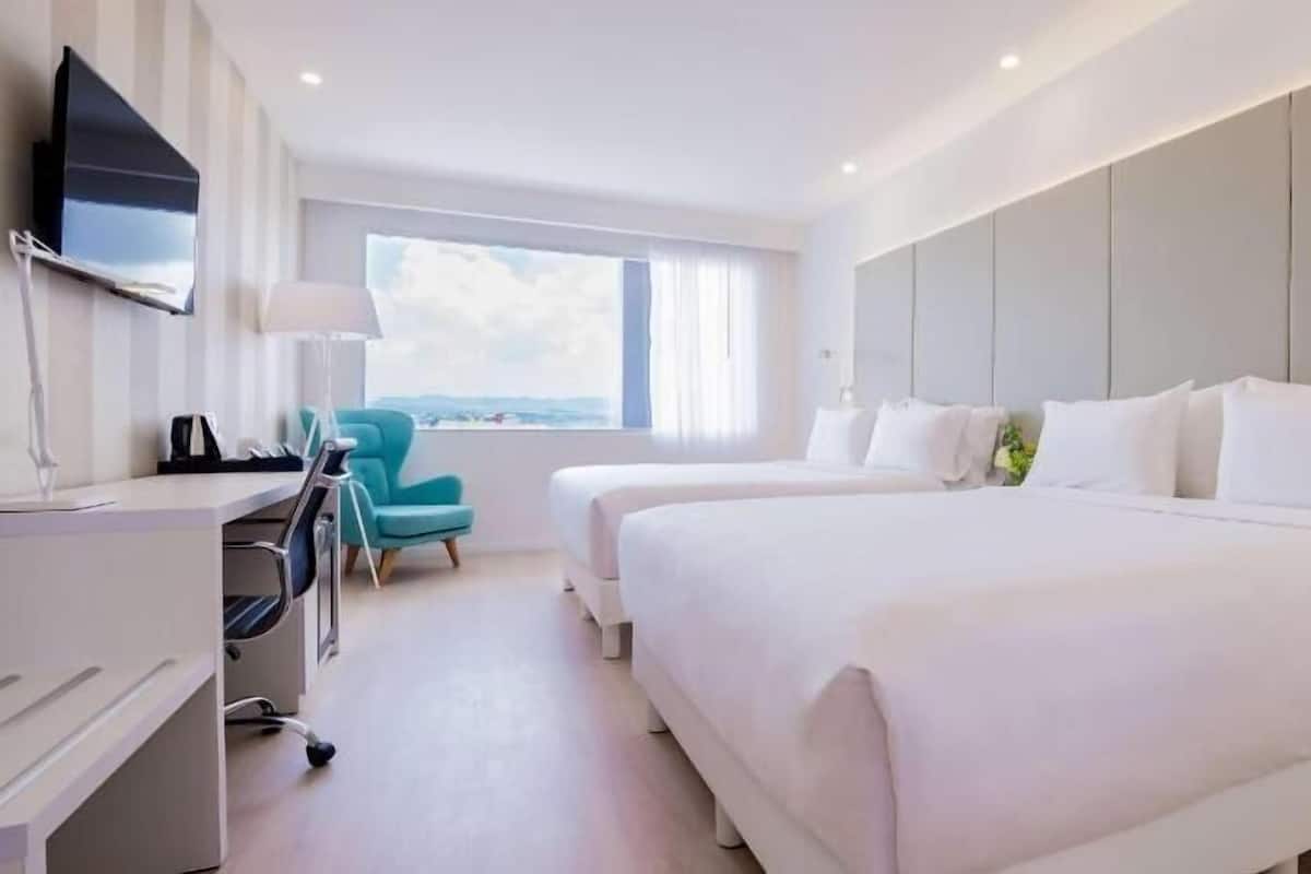A hotel room with two beds, a desk, a chair, and a TV.