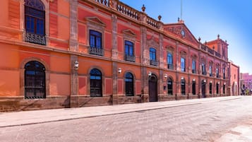A historic building with arched windows and balconies, a tiled courtyard, and a clear blue sky.