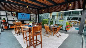 A modern outdoor dining area with wooden tables and chairs, potted plants, and a large digital sign displaying "NH SAN LUIS POTOSI". - NH San Luis Potosi (San Luis Potosi)