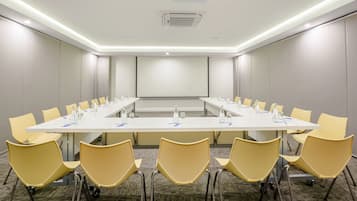 A conference room with a long table, yellow chairs, and a projector screen.