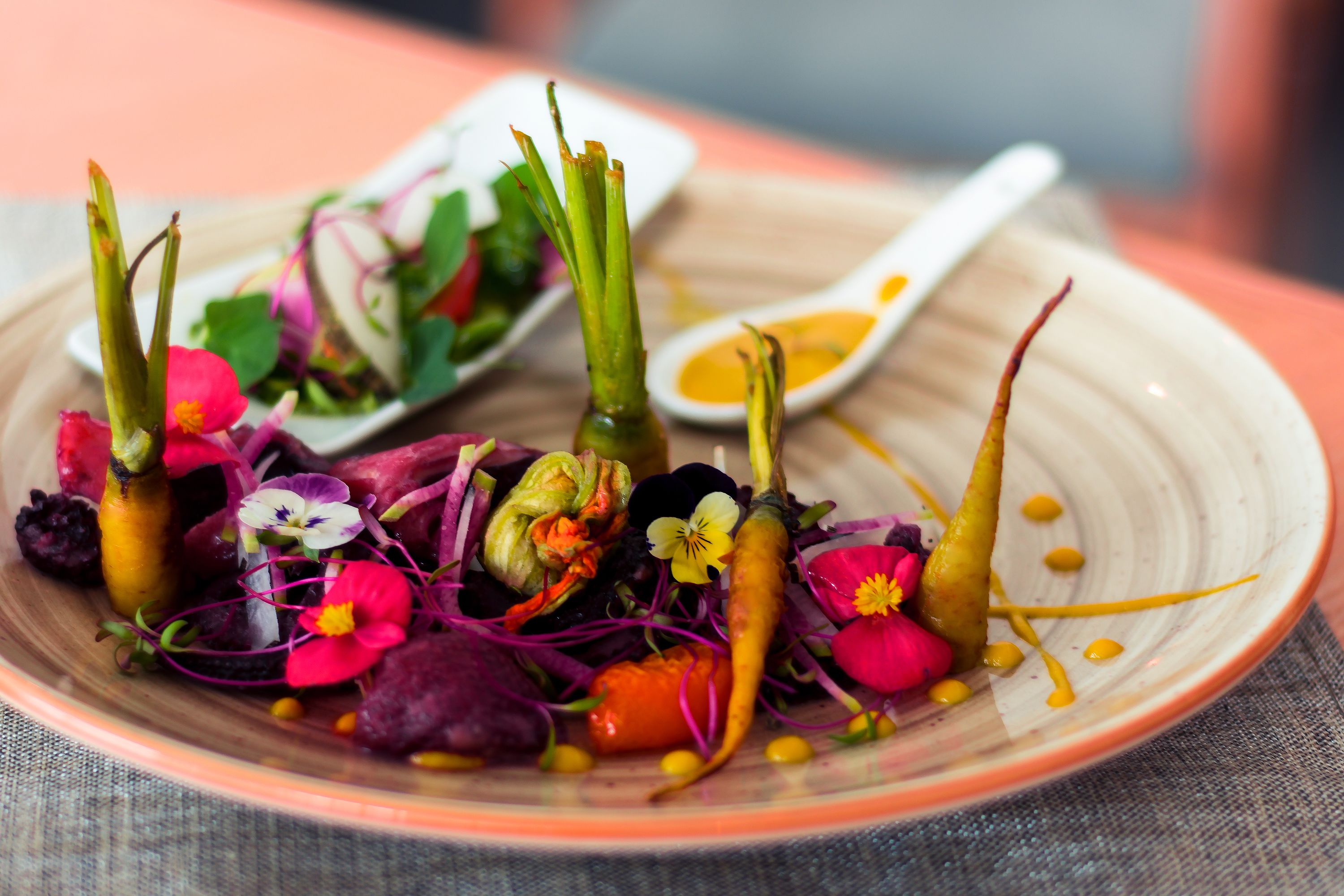 Un plato de verduras y flores coloridas con un recipiente pequeño de salsa amarilla.
