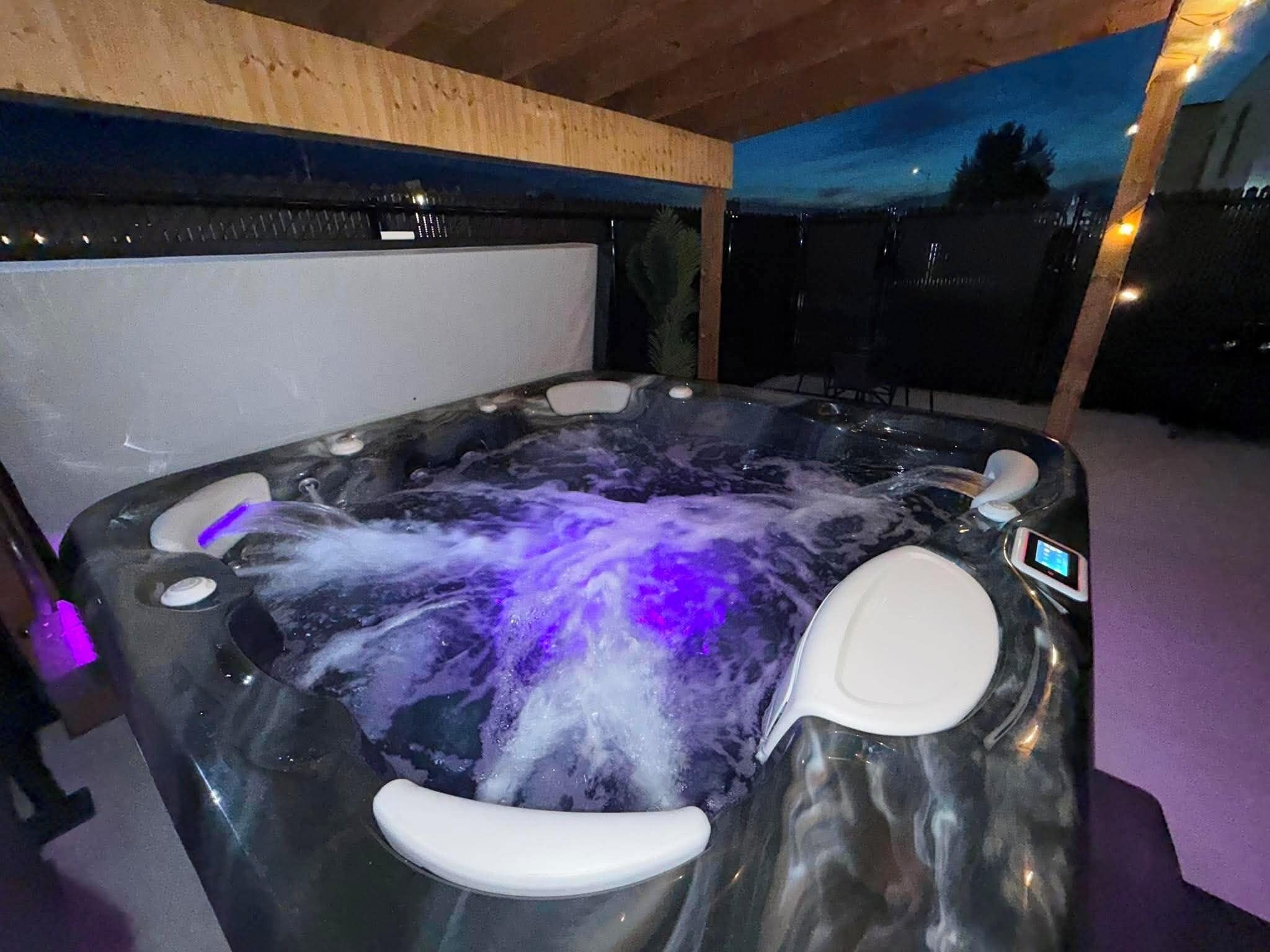 Un bain à remous doté d’un panneau de commande numérique, entouré d’une terrasse en bois et offrant une vue sur le ciel nocturne.