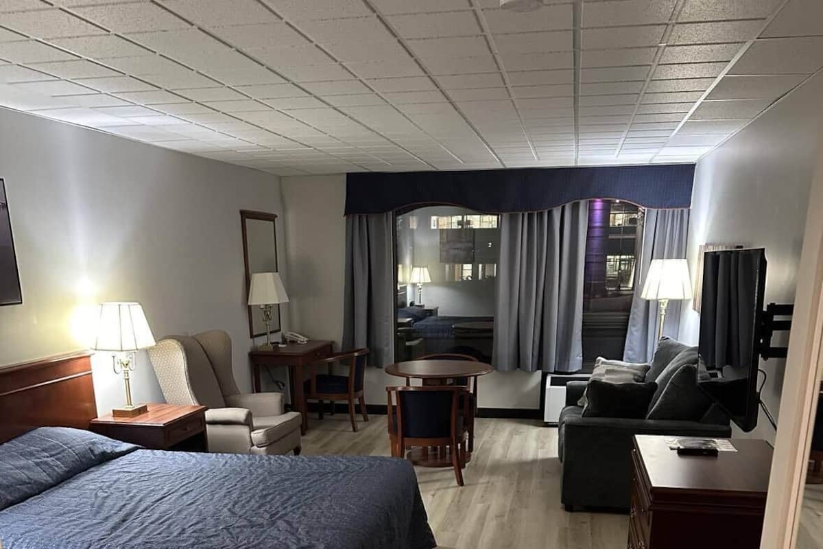 A hotel room with a large bed, a desk, a chair, a sofa, and a TV.