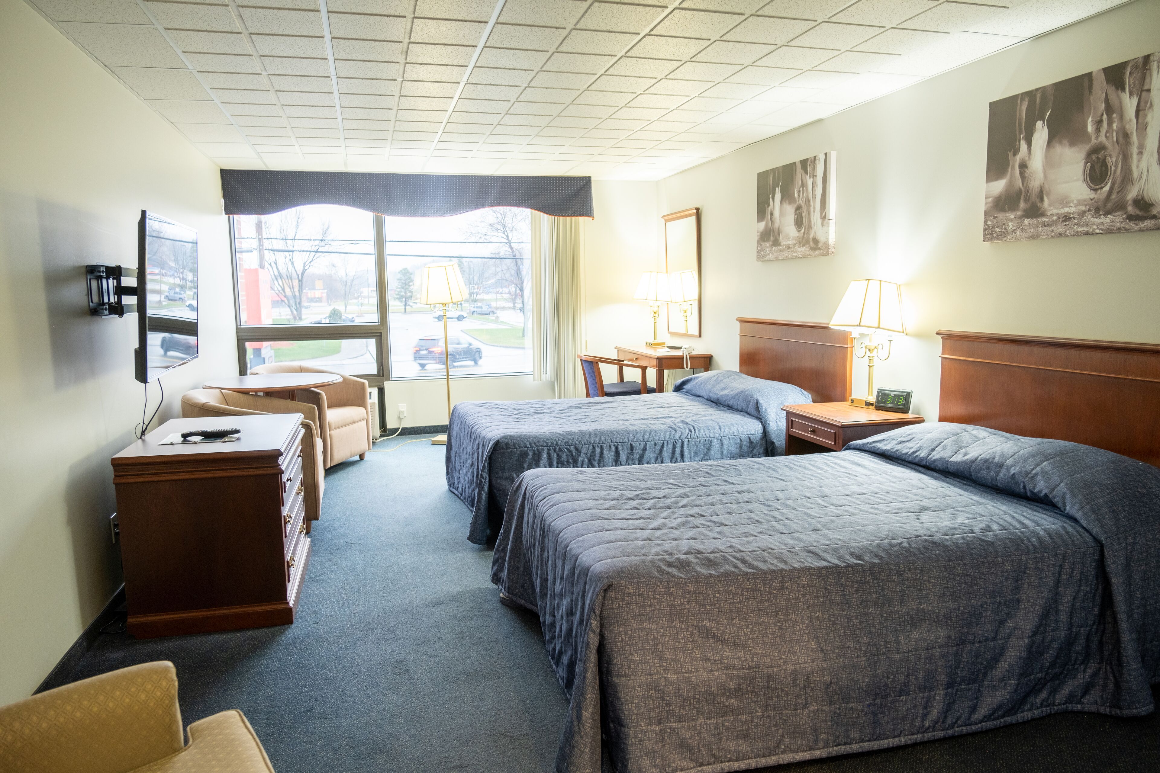 A hotel room with two beds, a desk, a chair, a dresser, and a television.