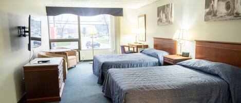 A hotel room with two beds, a desk, a chair, a dresser, and a television.