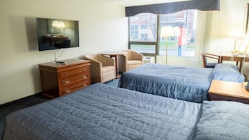 Habitación de hotel con dos camas, televisión, escritorio, silla y ventana con vista a edificios.