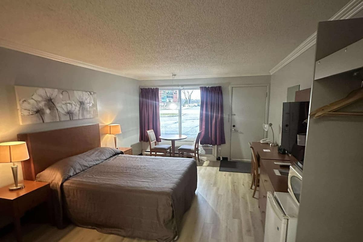 A hotel room with a bed, bedside tables, a desk, a chair, a TV, and a window with curtains.