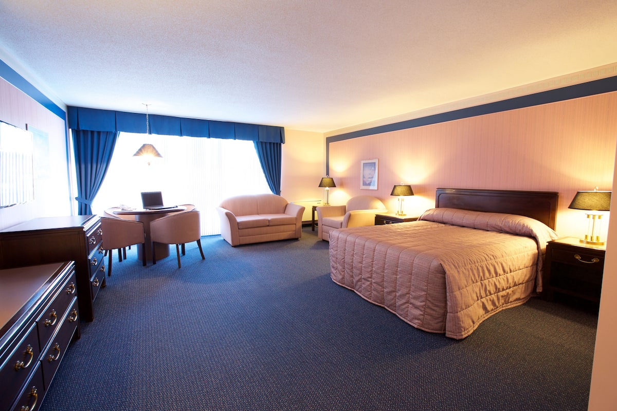 A hotel room with a large bed, two armchairs, a desk, and a dresser.