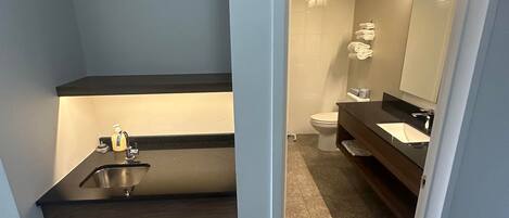 A modern bathroom with a dark countertop sink, a mirror, and a toilet.