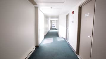 Un long couloir étroit, doté d’un sol recouvert de moquette et de murs blancs. Des portes se trouvent sur le côté droit, dont une porte portant le numéro 209.