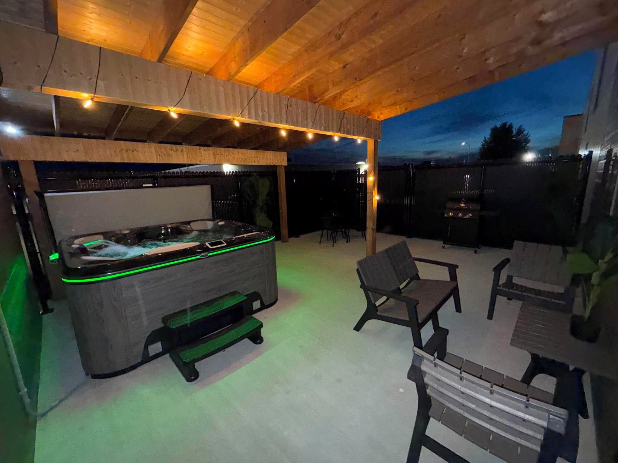 An outdoor patio with a hot tub, seating area, and a grill.