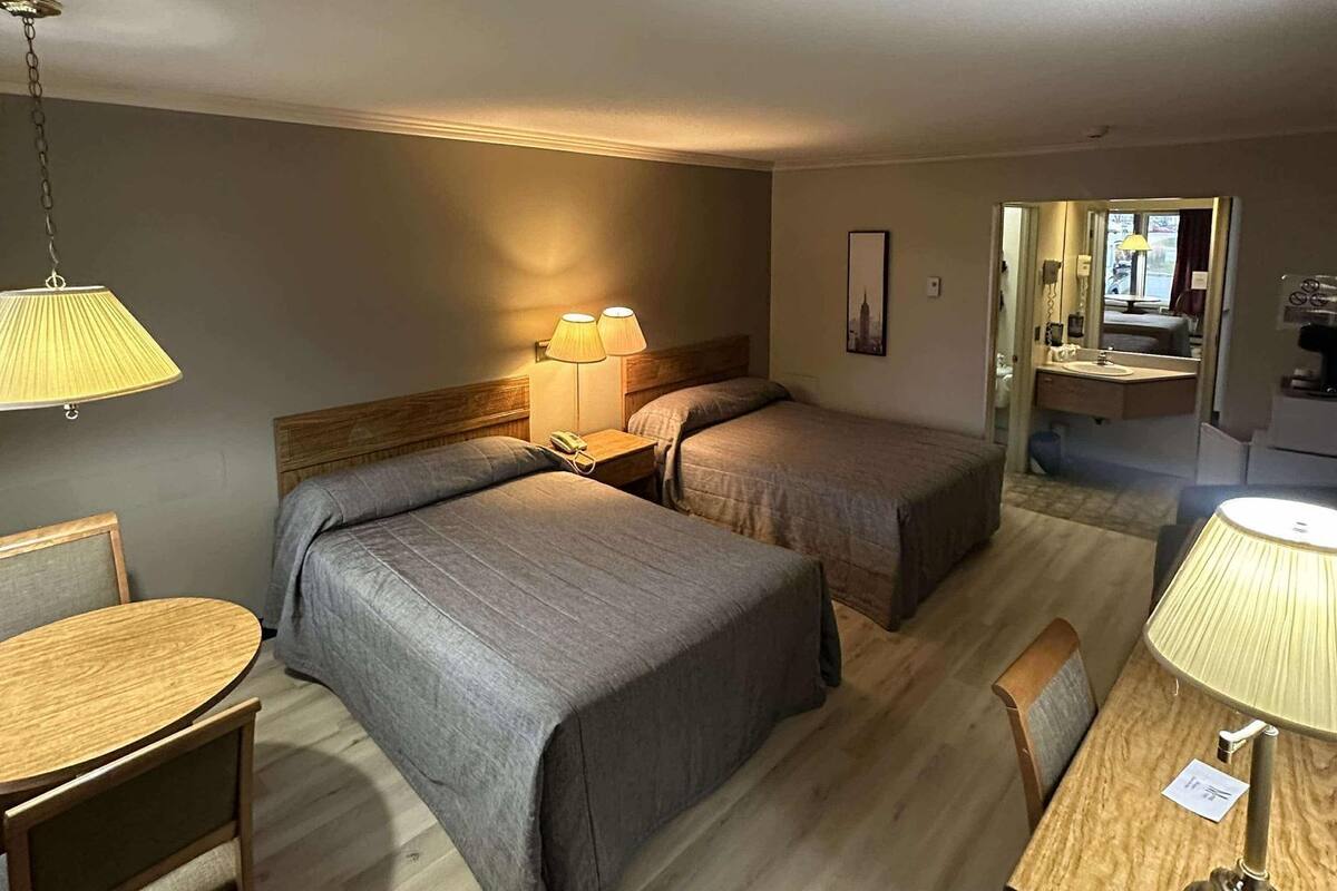A hotel room with two beds, a wooden desk, a chair, and a lamp.