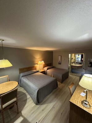 Habitación de hotel con dos camas, un escritorio de madera, una silla y una lámpara.