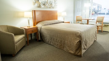 A hotel room with a large bed, two bedside tables, a chair, a small table, and a window with curtains.