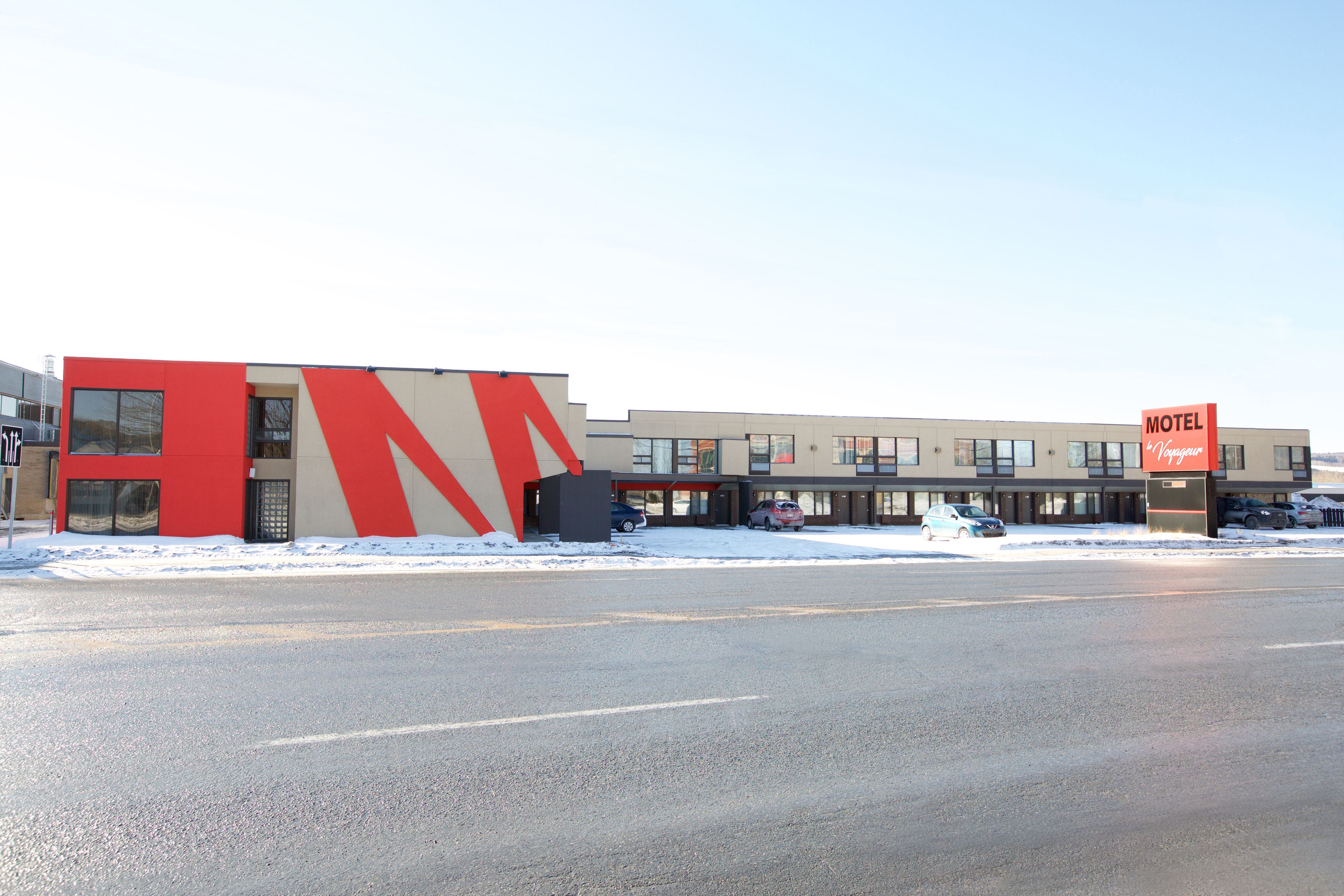 A modern motel with a red and beige facade, multiple windows, and a parking lot.