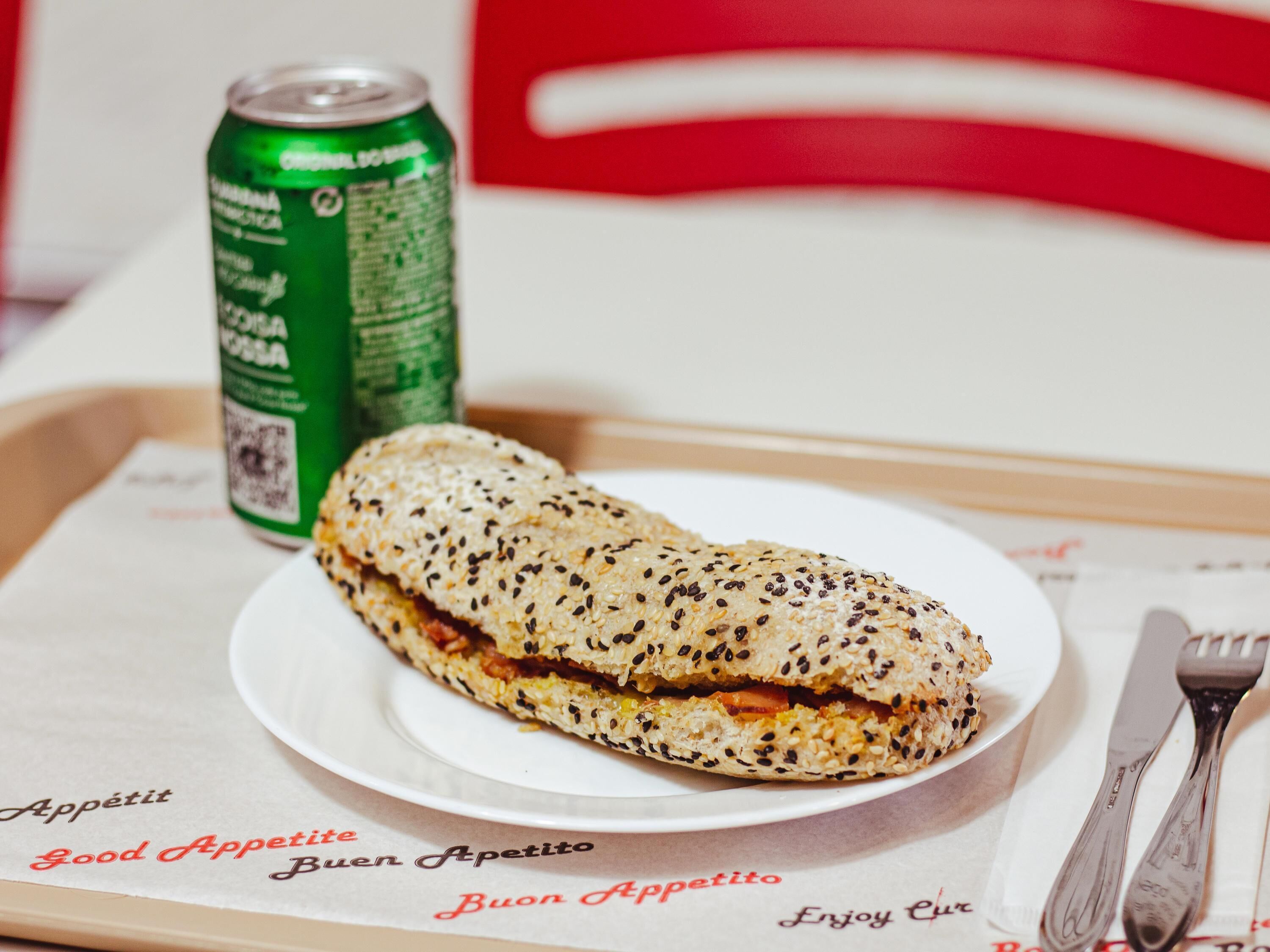 Un sándwich en un plato, con una lata de refresco al fondo.