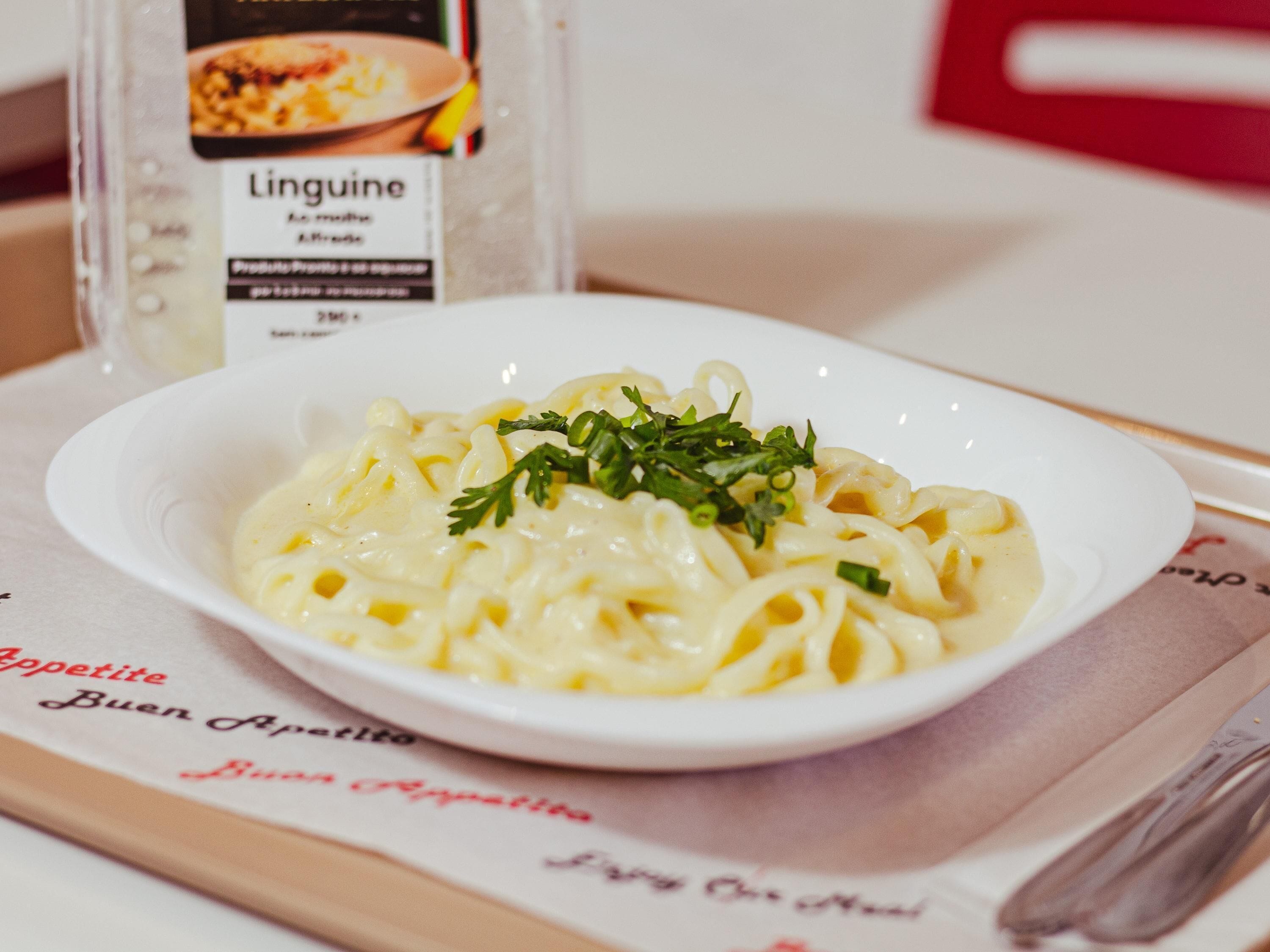 Un plato de pasta con guarnición sobre una mesa, junto a un menú y una botella de salsa para pasta Linguine.