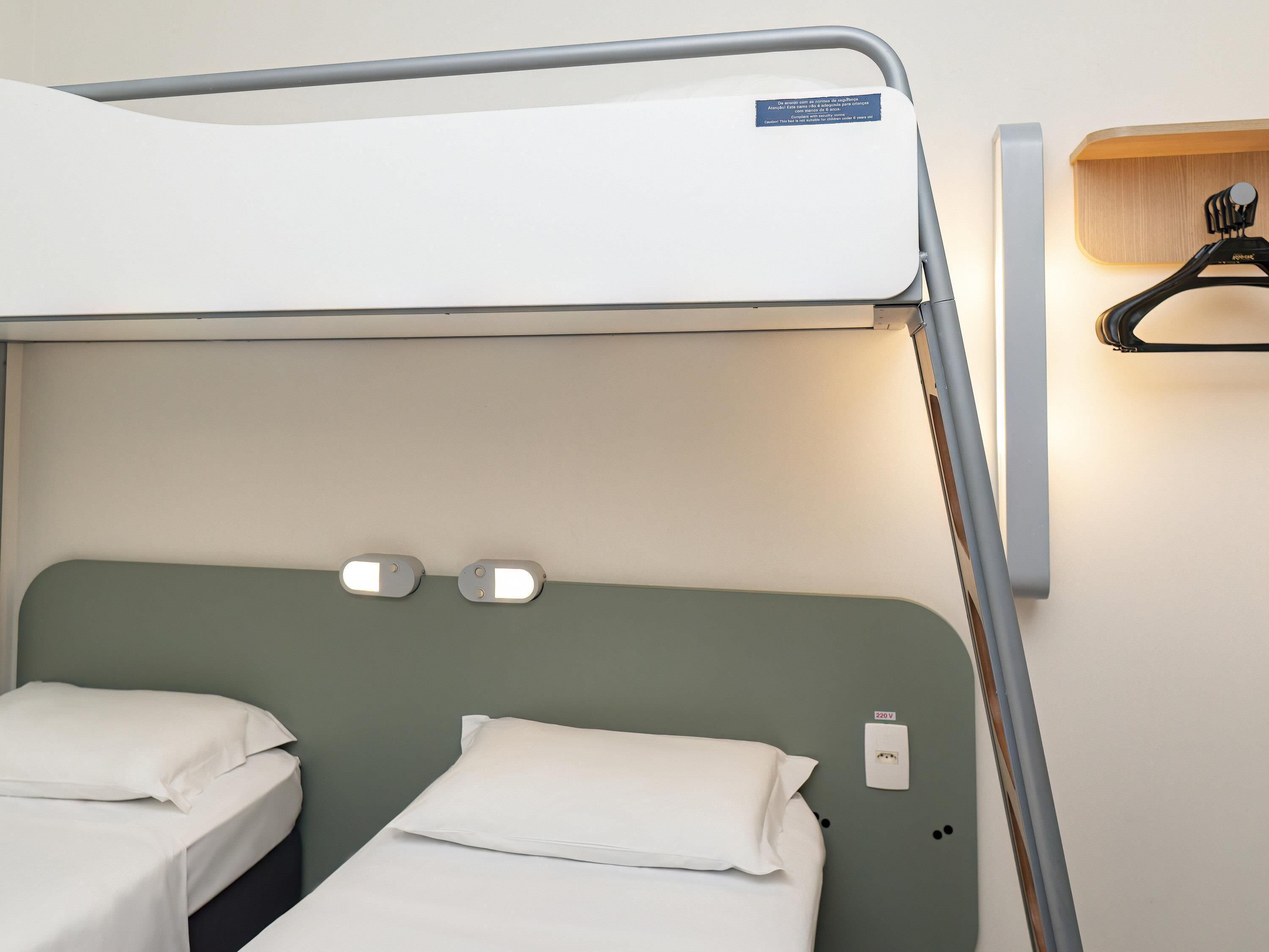 A bunk bed with a headboard, a wall-mounted light, and a power outlet.