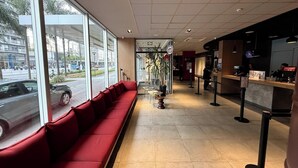 Ein modernes Interieur mit einer roten Sitzecke, einem Empfangsbereich und großen Fenstern mit Blick auf eine Straße.