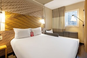 Une chambre d’hôtel avec un lit, une table de chevet, une lampe et une fenêtre avec des rideaux.