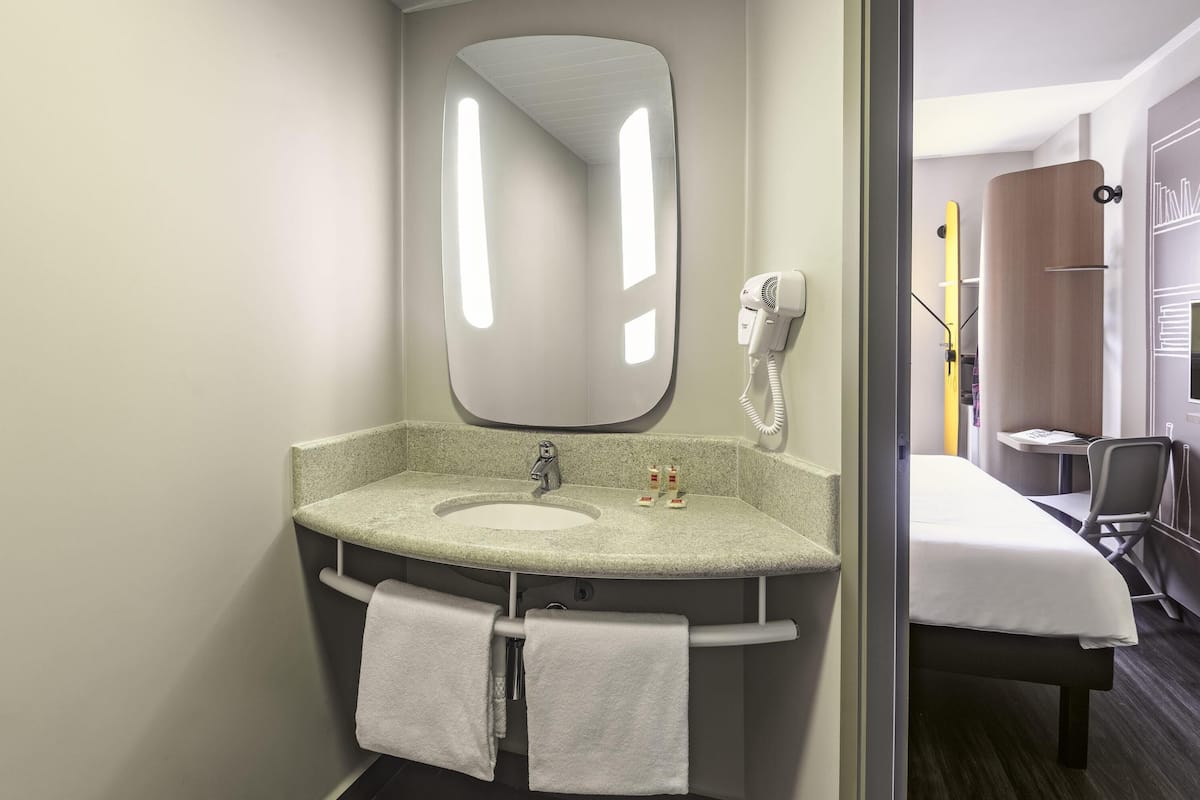 Une salle de bain équipée d’un lavabo, d’un miroir, d’un porte-serviettes et d’un sèche-cheveux fixé au mur.