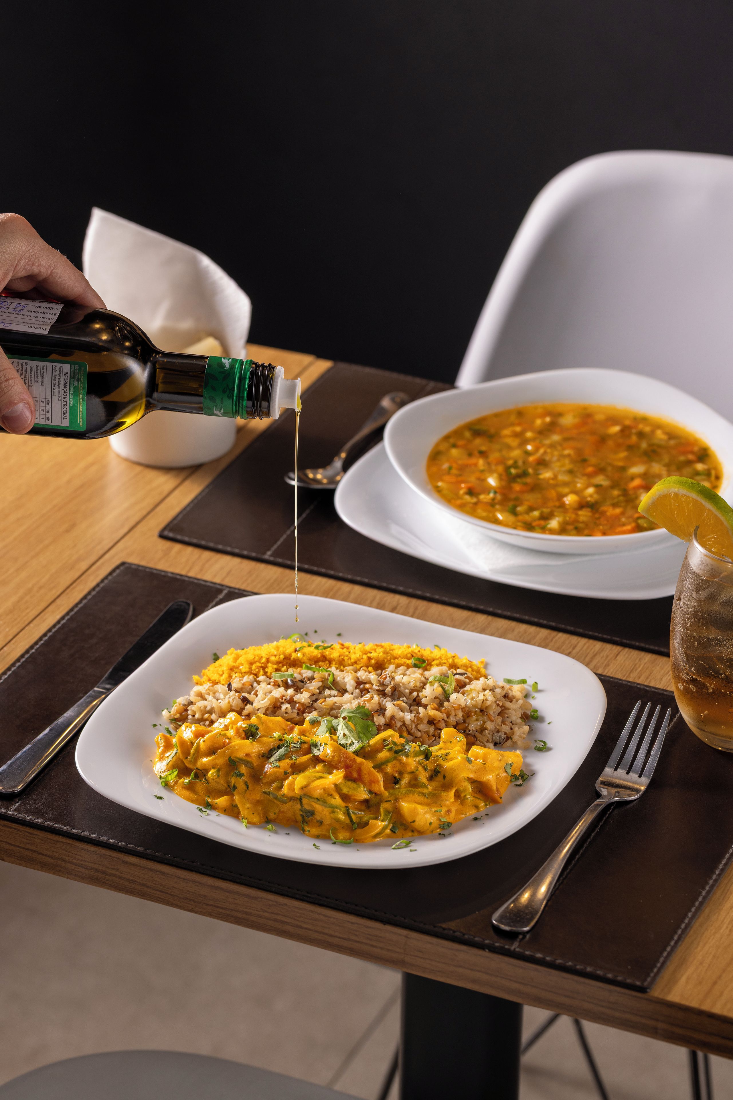 Een eettafel met een bord eten, een kom soep en een fles olie dat in wordt gegoten.