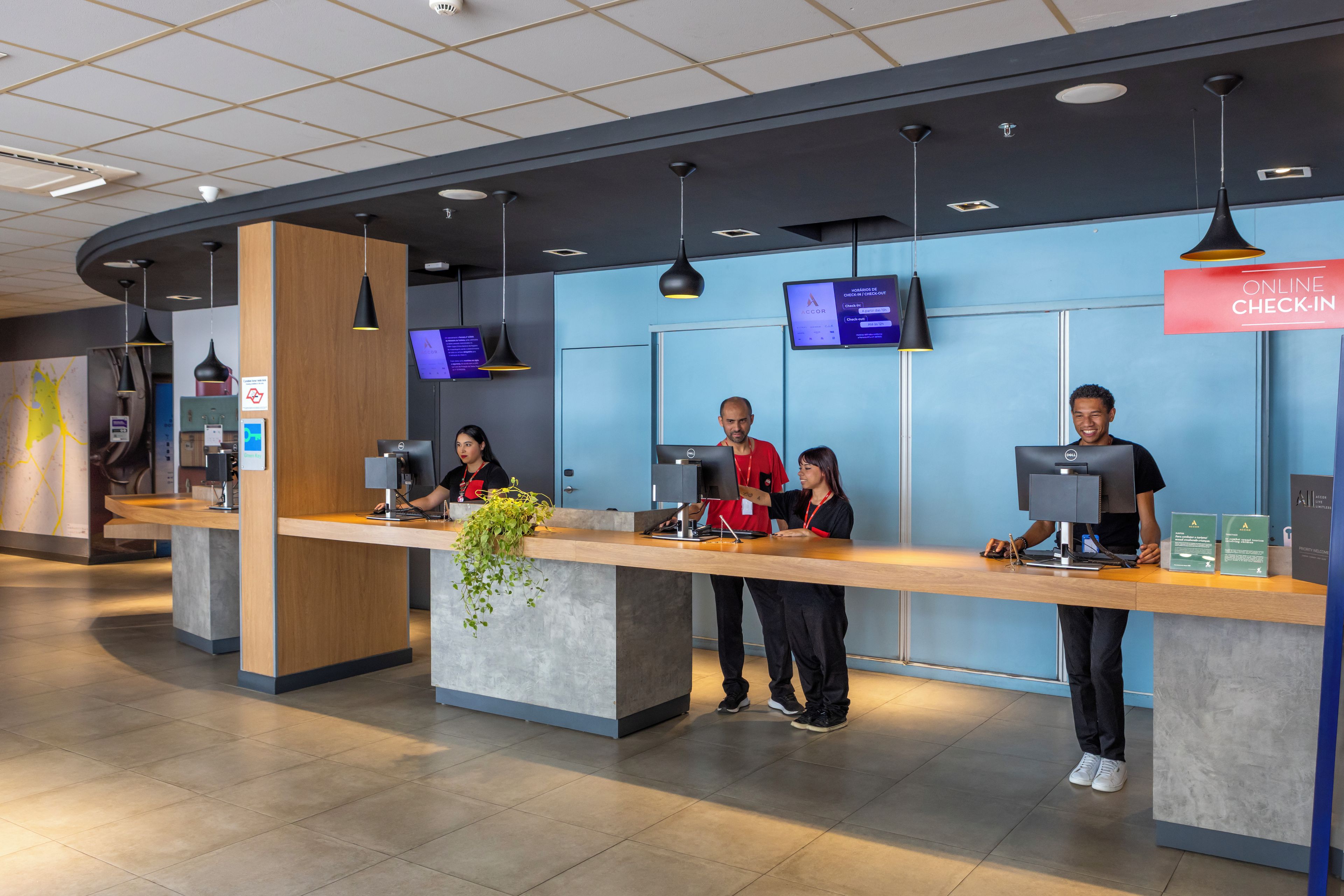 Un área de recepción moderna con pared azul, pantallas digitales y un cartel que indica registro en línea.