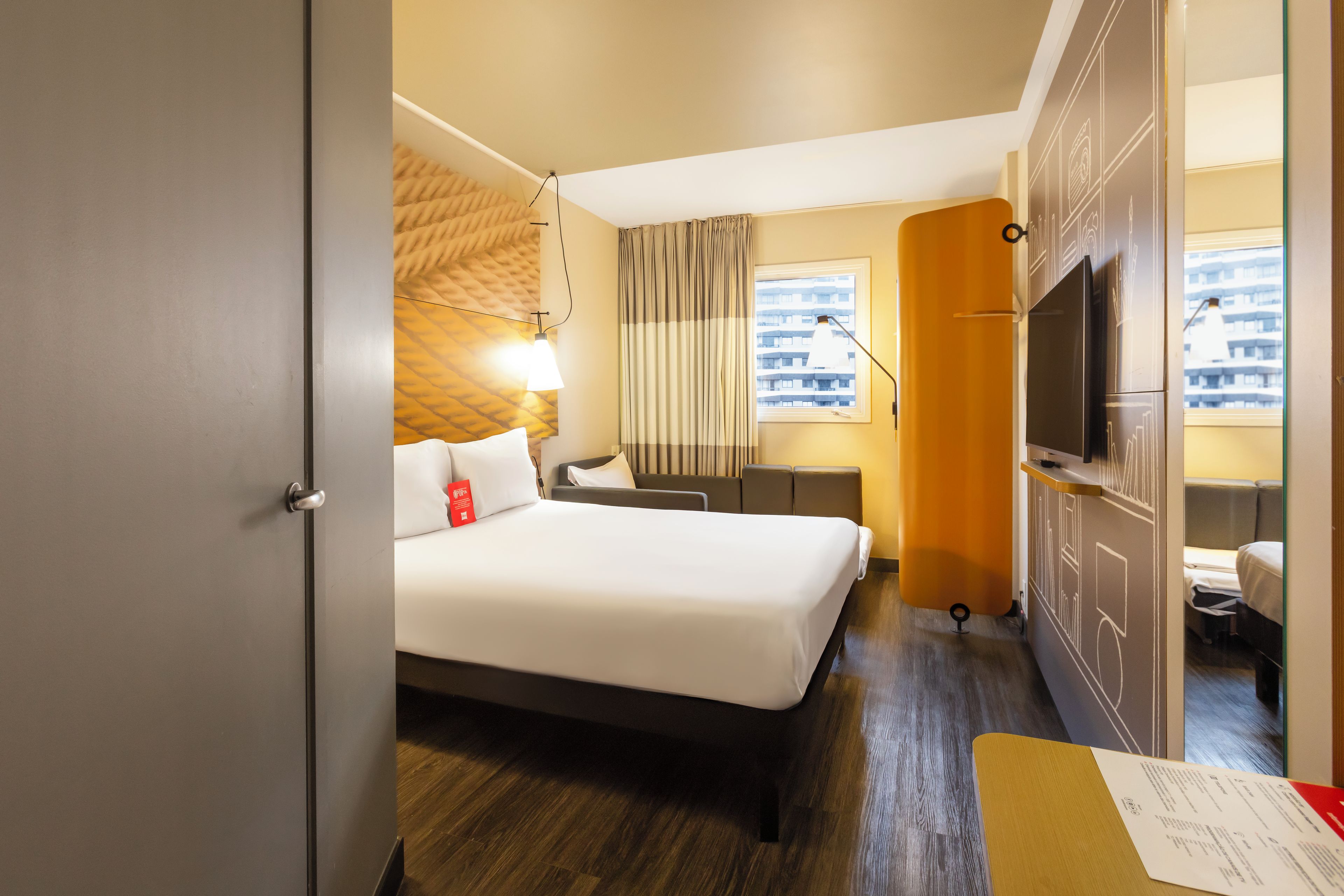 Habitación de hotel con cama, escritorio, televisor y ventana con vista a la ciudad.